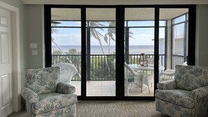A room with two patterned armchairs, a small table, and a view of the ocean through large sliding glass doors.