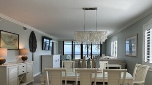 A spacious dining area with a marble countertop, white furniture, and a view of the ocean through large windows.