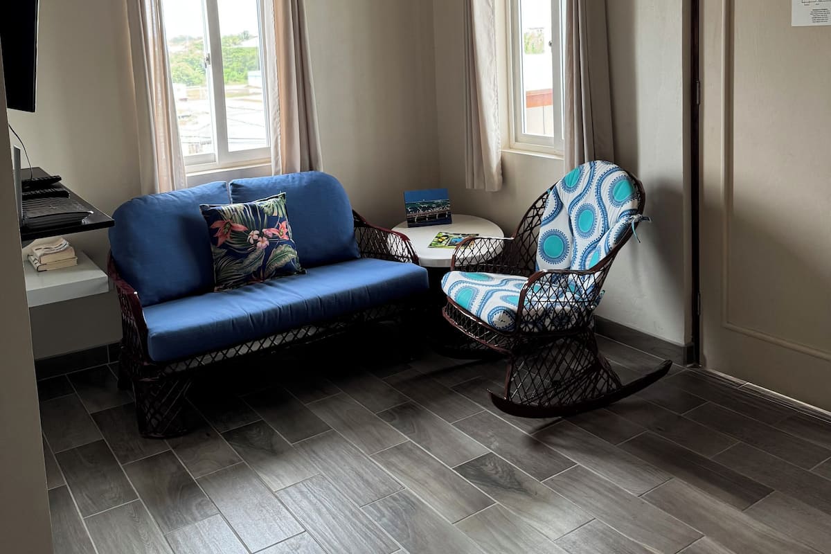 Una habitación con un sofá azul, un sillón estampado, un ventilador de techo y un aire acondicionado.
