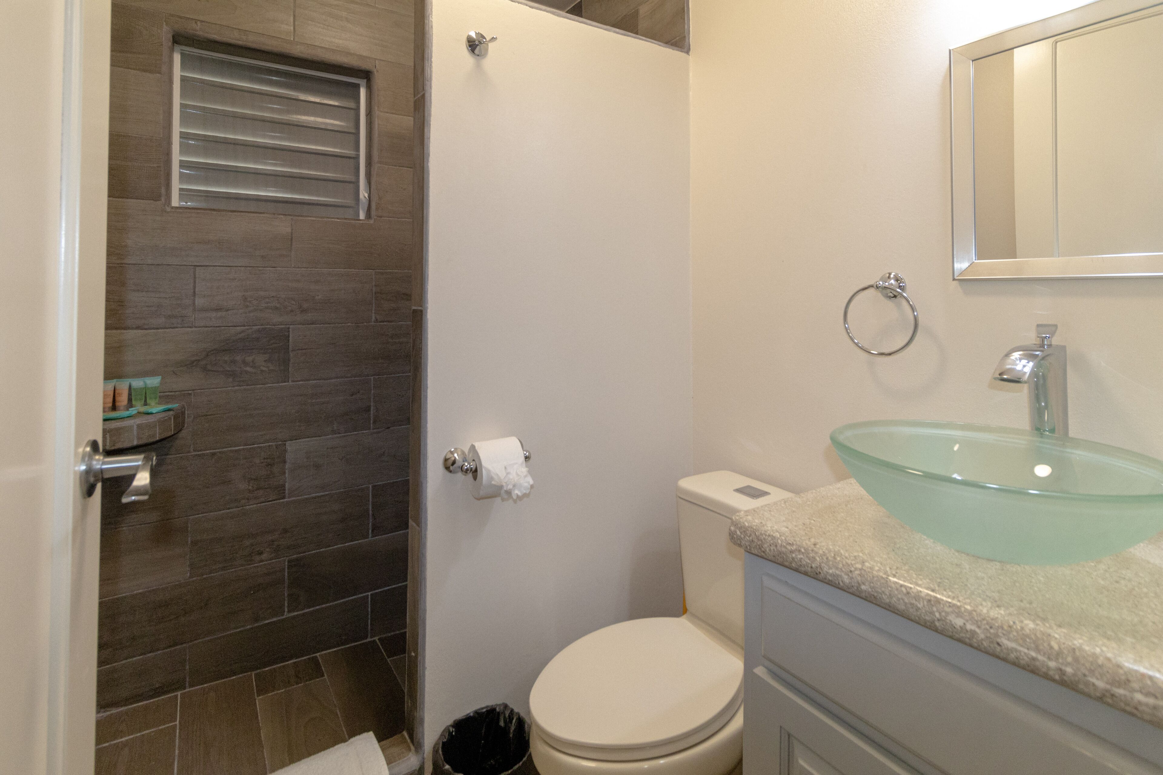 A bathroom with a glass sink, a toilet, and a shower area.