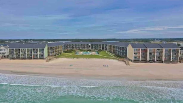 Un hotel frente al mar con un patio central, varias habitaciones y una playa de arena.