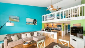 Un salón moderno con una pared de acento color turquesa, un sofá marrón, una mesa de centro de madera y una zona de cocina con barra.