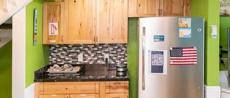 A compact kitchen with wooden cabinets, a stainless steel refrigerator, and a tiled floor.