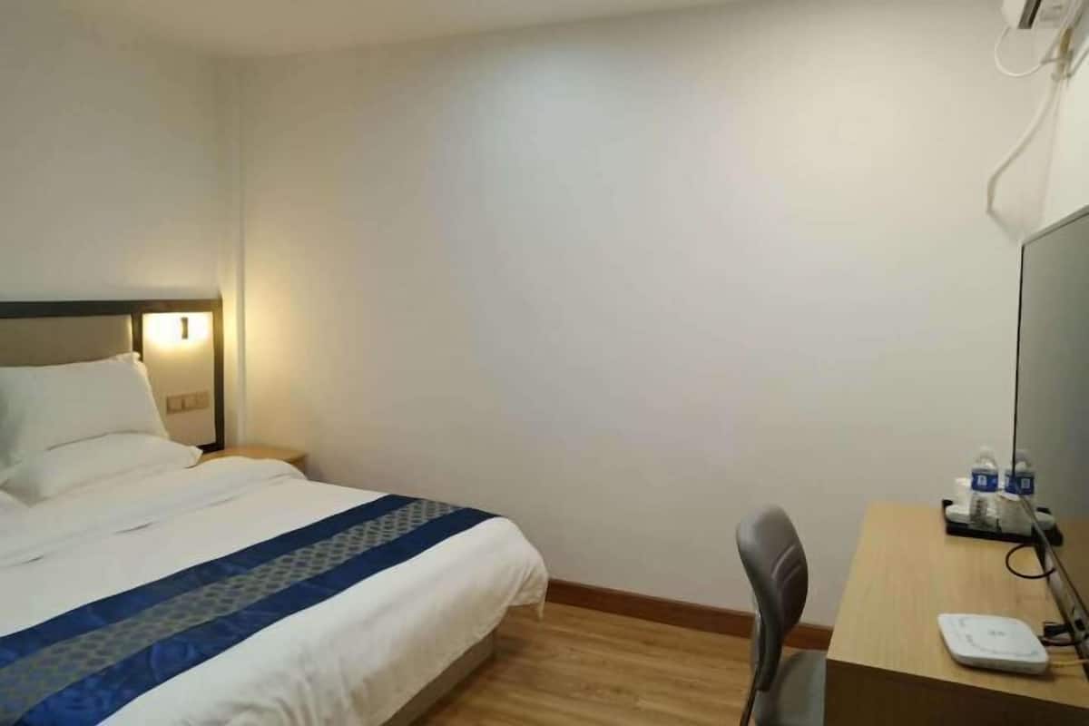 A hotel room with a bed, a desk with a chair, a scale, and a mirror.