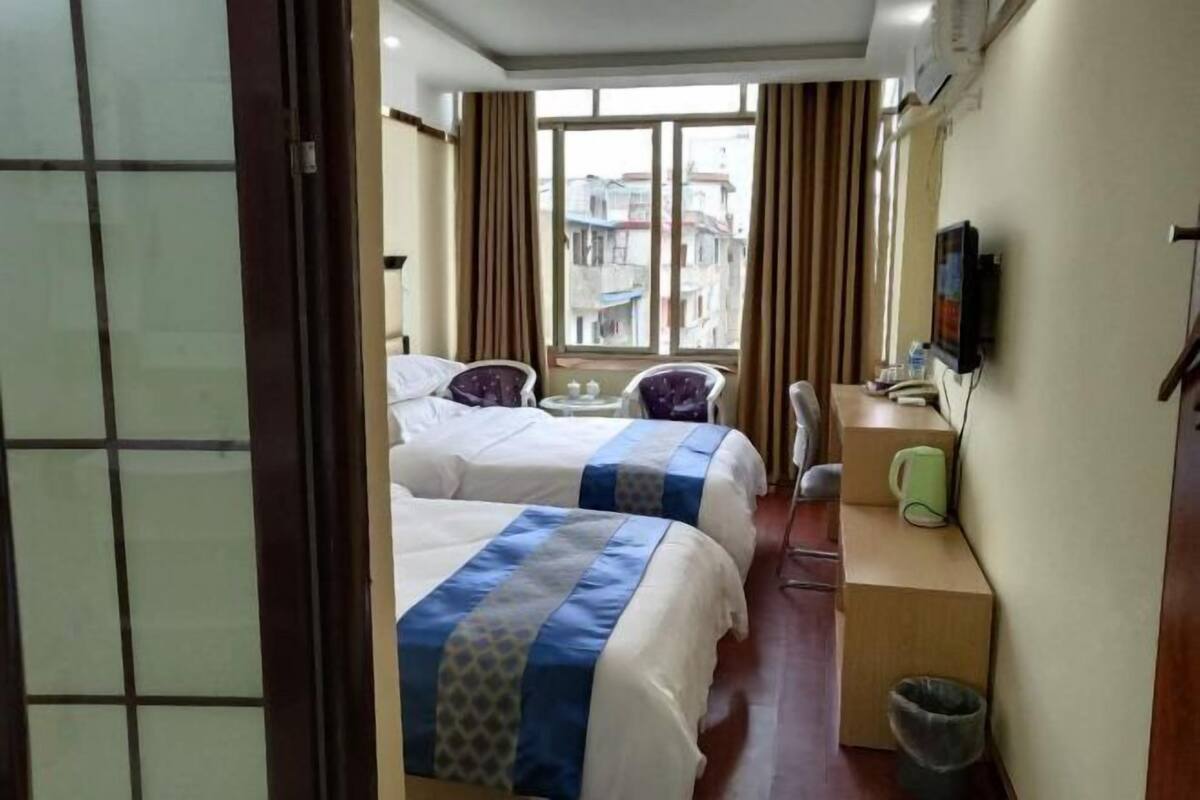 A hotel room with two beds, a desk, a chair, a TV, and a window with a view of buildings.