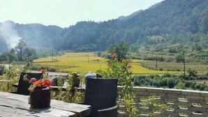 Un’area salotto esterna in stile rustico con una sedia in vimini e un tavolo, con vista su un paesaggio collinare con campi e una montagna in lontananza.