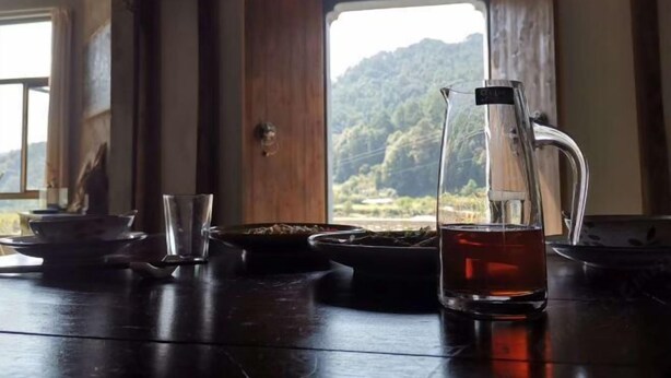 Un tavolo con una caraffa di tè, un bicchiere e stoviglie, con vista su una foresta attraverso una finestra.