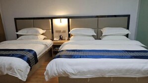Camera d'albergo con due letti singoli e un letto matrimoniale, ognuno con biancheria da letto bianca e un poggiatesta. È presente un comodino con una lampada e un telefono.