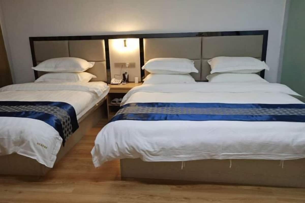 A hotel room with two single beds and one double bed, each with white bedding and a headboard. There is a nightstand with a lamp and a phone on it.
