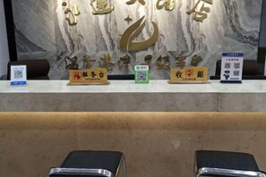 A reception desk with a marble wall background, nameplates for reception and cashier, and a QR code for information. - Yongda Hotel (Hengfeng)