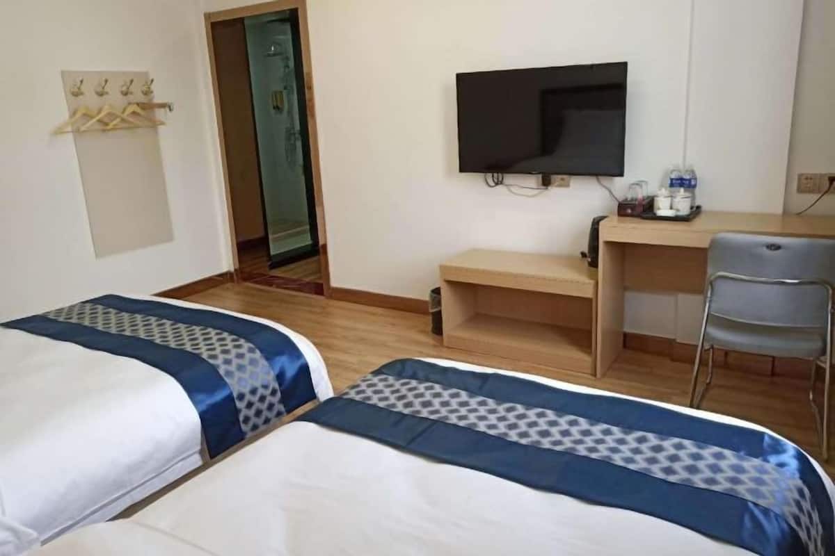 A hotel room with two beds, a desk, a chair, a television, and a coat rack.