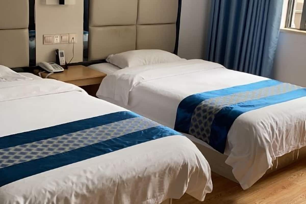 A hotel room with two beds, a bedside table with a phone, and a window with curtains.