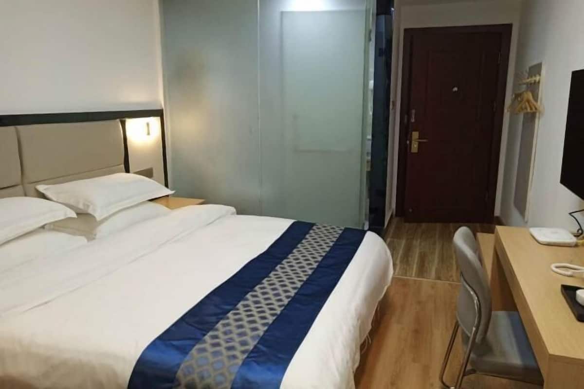 A hotel room with a bed, a desk with a telephone, a chair, and a door.