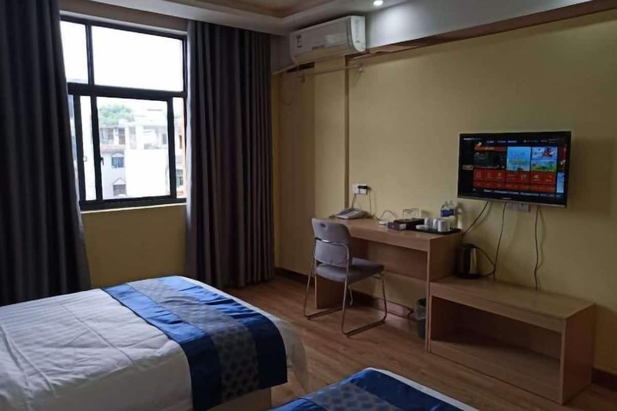 A hotel room with a bed, a desk, a chair, a TV, and a window.