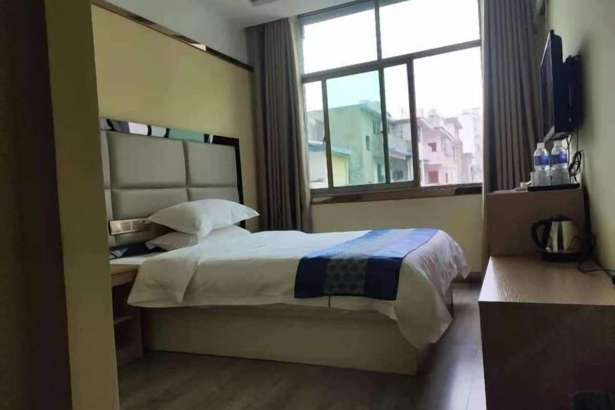 A hotel room with a bed, a desk, a television, and a window with a view of buildings.