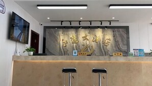 Una reception con parete in marmo e scritte dorate, due sgabelli da bar, un televisore a parete e una pianta in vaso.