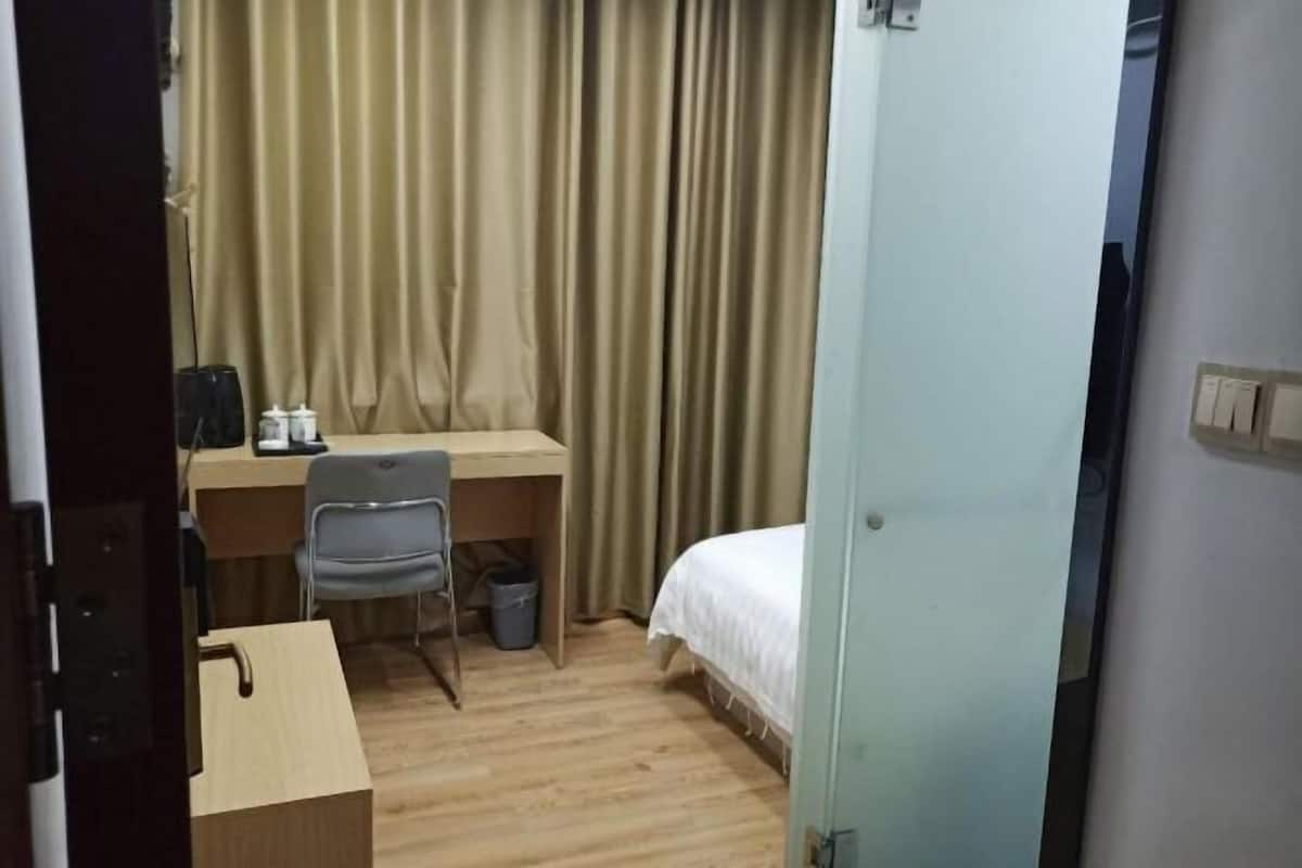 A room with a bed, a desk with a chair, and a curtain.