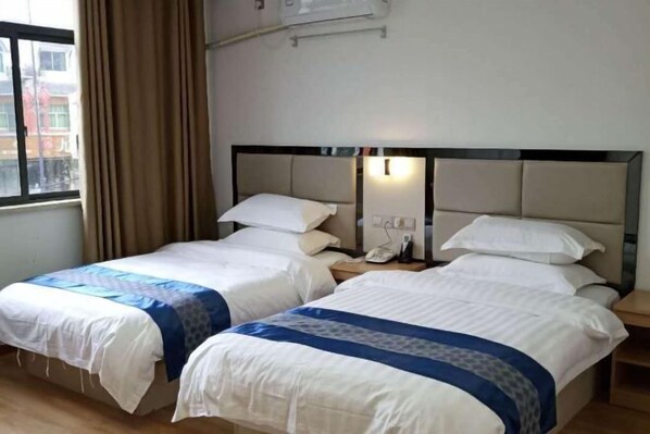 Quarto de hotel com duas camas, uma janela com cortinas, mesa de cabeceira com telefone e ar-condicionado fixado na parede.