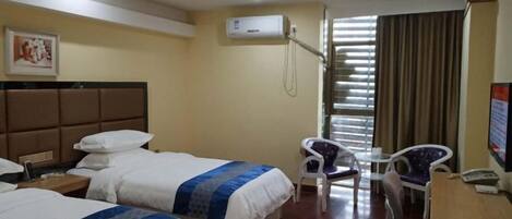 Une chambre d’hôtel avec deux lits, un bureau, une chaise, un appareil de climatisation et une fenêtre avec des stores.