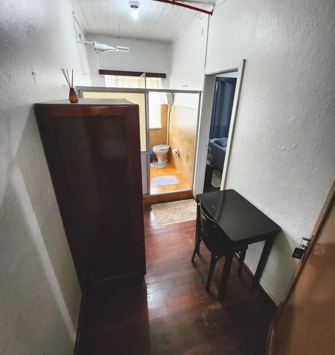 Un couloir étroit avec un meuble en bois, une petite table et une vue sur une salle de bain équipée de toilettes et d’une douche.