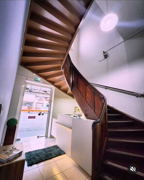 A modern interior with a wooden staircase, a reception desk, and a view of the street outside. - Hotel Real Koerich 24h (Rio do Sul)