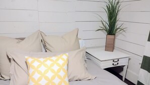 Un letto con biancheria beige, un cuscino bianco con motivo giallo e un comodino con una pianta in vaso.