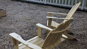 Una poltrona Adirondack in legno in un parco, con pacciamatura al suolo e una recinzione di legno bianco sullo sfondo.