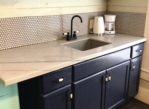 Sink and coffee maker sit atop a countertop with a patterned backsplash and sleek cabinets.