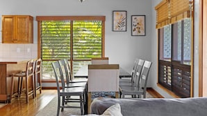 A modern kitchen with wooden cabinets, a dining area with chairs, a ceiling fan, and large windows with blinds. - Walk to Beach! HUGE 5 bedroom, 5 bath with Pool!! (Kailua-Kona)