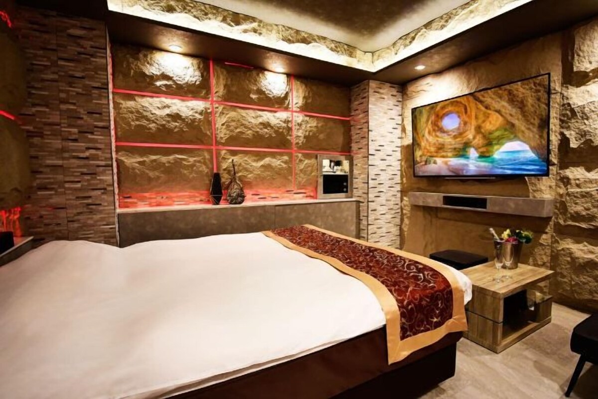 A hotel room with a large bed, a TV mounted on the wall, and a stone-textured wall.