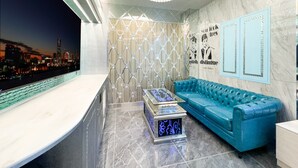 Un intérieur moderne avec un canapé bleu, une table basse en verre, un lustre et une vue sur le paysage urbain.