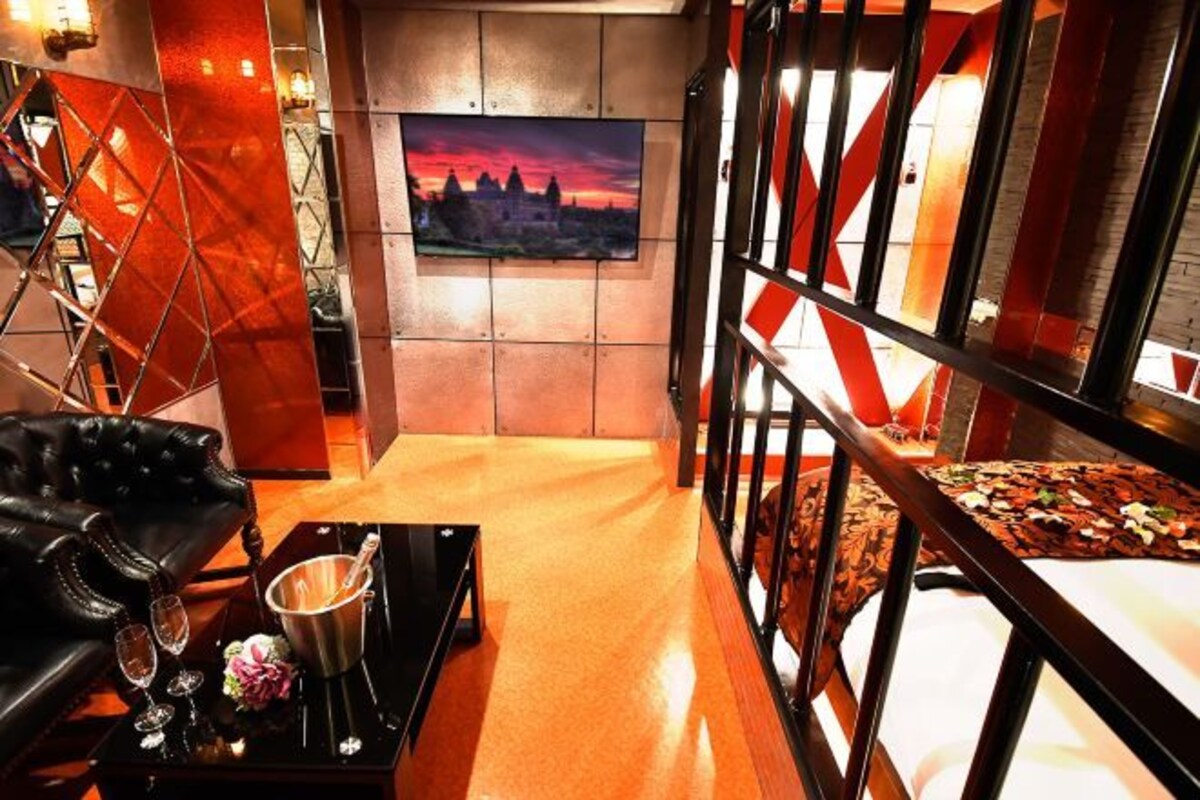 A room with a bed, a black leather sofa, a small table with a drink, and a painting on the wall.