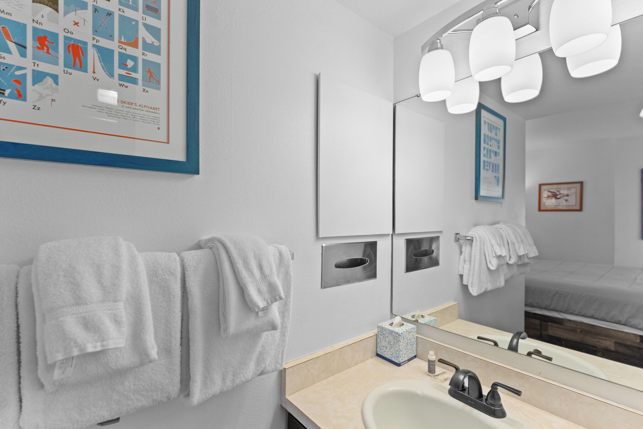Un baño moderno con un espejo grande, varias luces y toallas ordenadas.