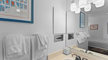 Un baño moderno con un espejo grande, varias luces y toallas ordenadas.