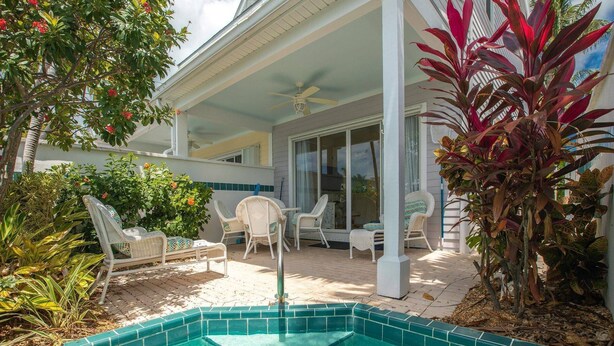 Un espace piscine avec un jacuzzi, entouré de chaises en osier blanc et doté d’un patio couvert.