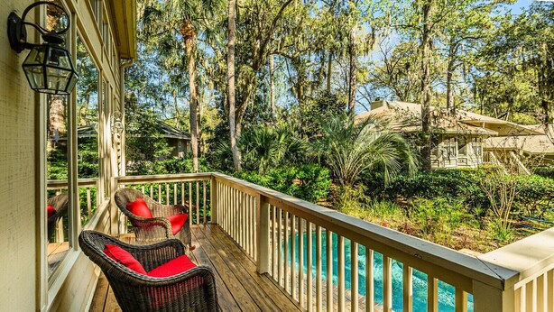 Une terrasse en bois, dotée de chaises en osier, et offrant une vue sur une piscine entourée d’arbres.