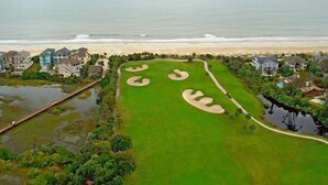 Vue aérienne d’un terrain de golf avec des bunkers, une plage et des immeubles résidentiels.
