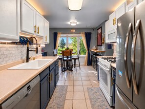 Une cuisine moderne avec des meubles blancs, des appareils en acier inoxydable et une vue sur l’extérieur.
