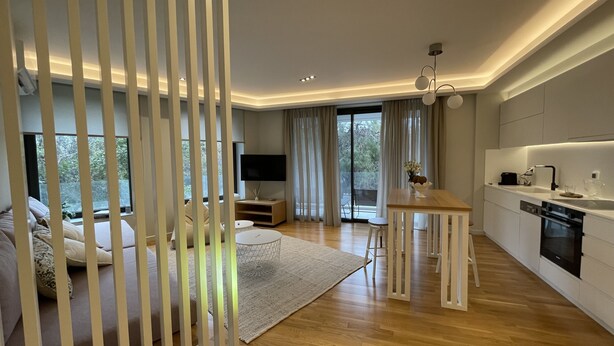 A modern living room with a sofa, a coffee table, and a TV. There is a kitchen area with a dining table and a sink. - Acropolis Residence with 360-Degree Athens City Views Rooftop (Athina)