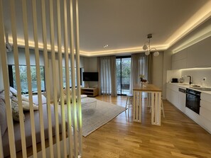 En moderne stue med sofa, sofabord og fjernsyn. Der er et køkkenområde med spisebord og vask.