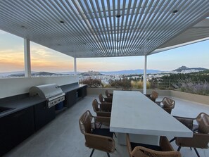 En uteplats med grill, matbord och stolar, med utsikt över en stad och berg.