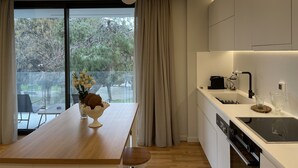 A modern kitchen with a wooden dining table, a vase of flowers, and a view of a park through large windows. - Acropolis Residence with 360-Degree Athens City Views Rooftop (Athina)