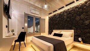 Un dormitorio moderno con una pared de acento de piedra, una cama grande, una silla y un escritorio con un ordenador portátil.