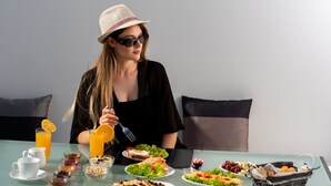 Una mesa de comedor con diversos alimentos para desayuno, incluyendo platos de comida, una cesta de pan y un vaso de zumo de naranja.
