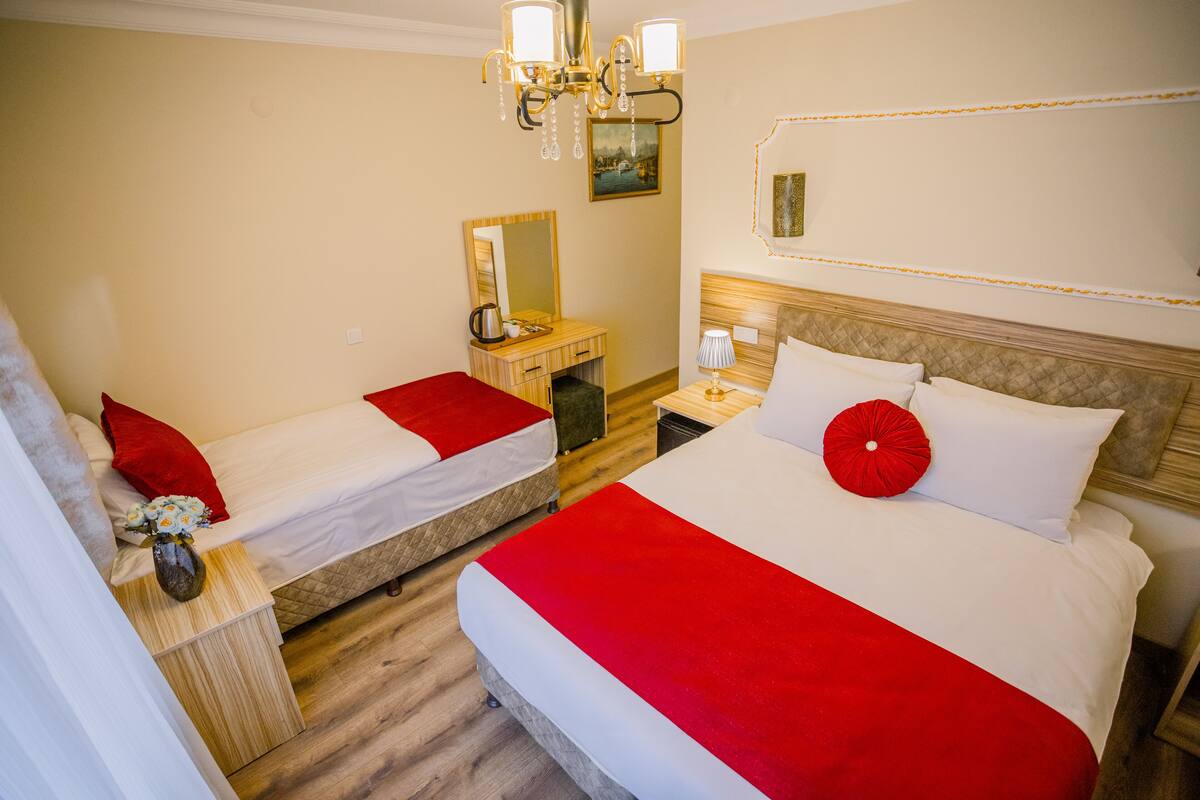 A hotel room with two beds, a wooden dresser, a mirror, a chandelier, and a painting on the wall.