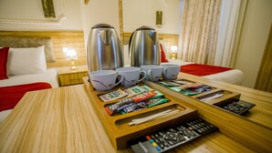 A hotel room with a wooden table, two electric kettles, multiple cups, a tray with snacks, and a remote control. - Gulec Konak Hotel (Istanbul)