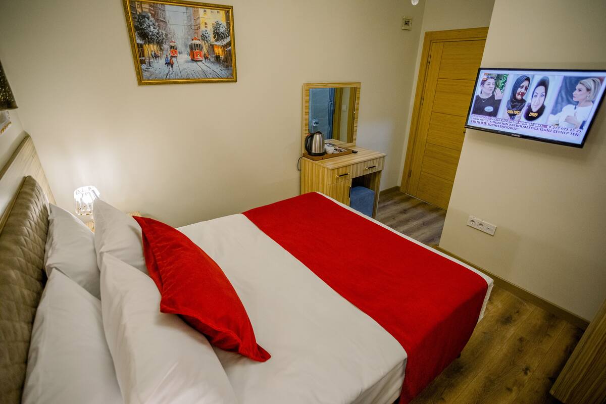 A hotel room with a bed, a wooden desk, a television, and a painting on the wall.