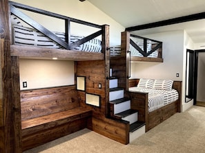 Een slaapkamer met een meerlaags stapelbed, houten balken en een trap.