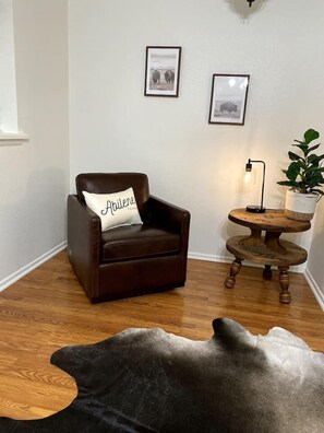 A room with a brown leather armchair, a small wooden side table with a lamp, and a framed picture on the wall.