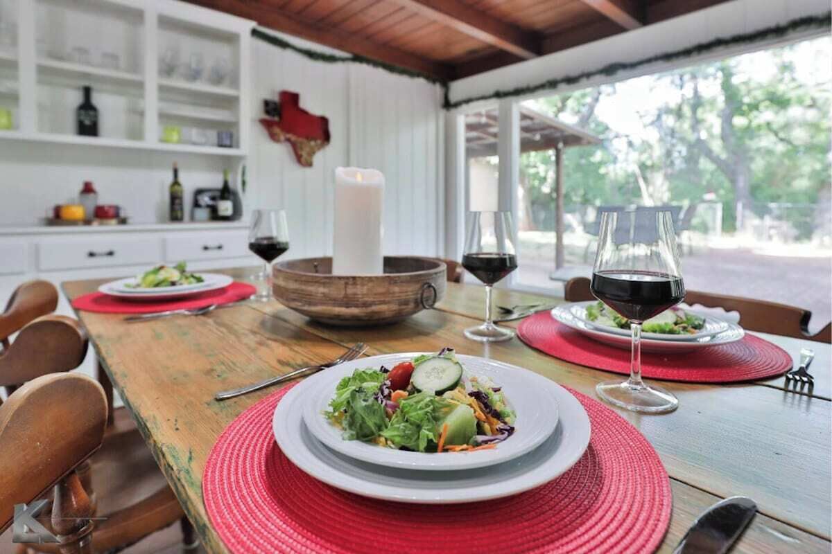 Een eettafel gedekt met saladeschotels, wijnglazen en een kaarsdecoratie.